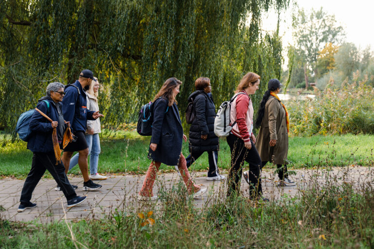 Groep mensen wandelt op een pad door een groen park, omgeven door bomen.