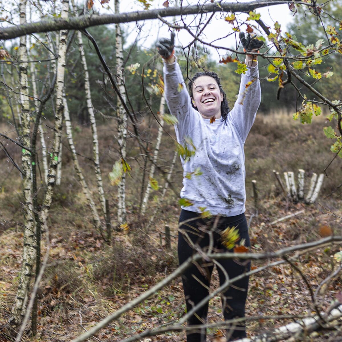 Persoon in bos werkt lachend aan snoeien van takken in herfstig landschap.