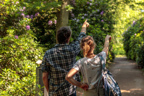 Een man en vrouw wijzen naar iets in een groene, bloemrijke tuin.