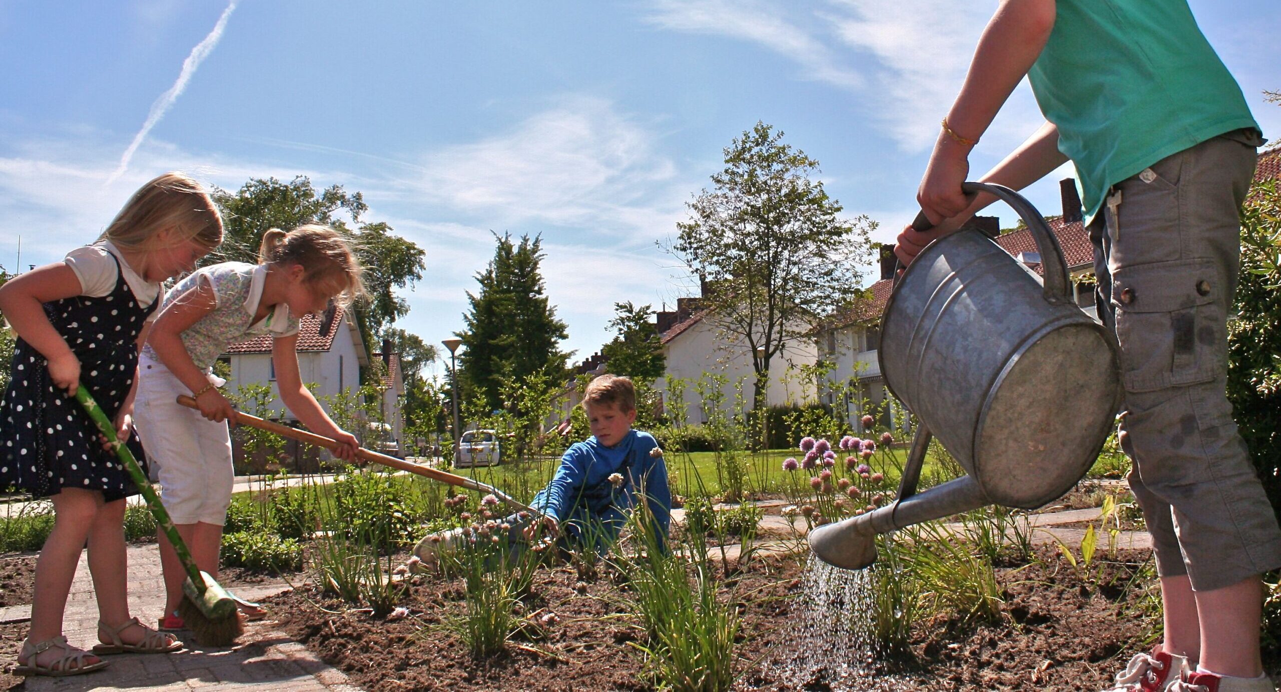 Kinderen tuinieren samen in een zonnige tuin, gieter en planten zichtbaar.