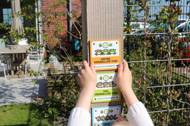 Een kind hangt borden op voor een amfibieën- en egelvriendelijke tuin.