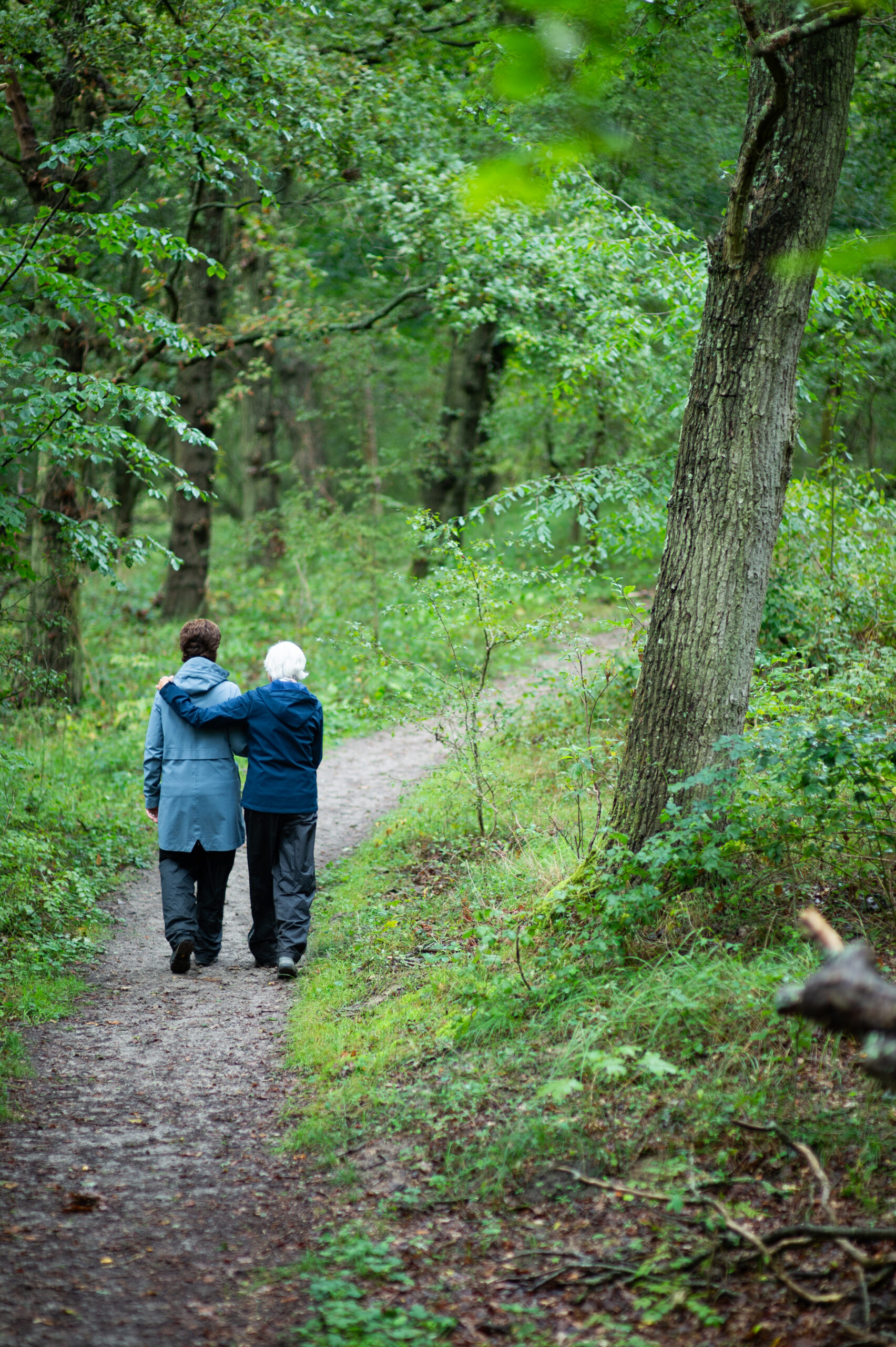 Twee mensen wandelen samen op een bospaadje, omringd door groen bladerdek.