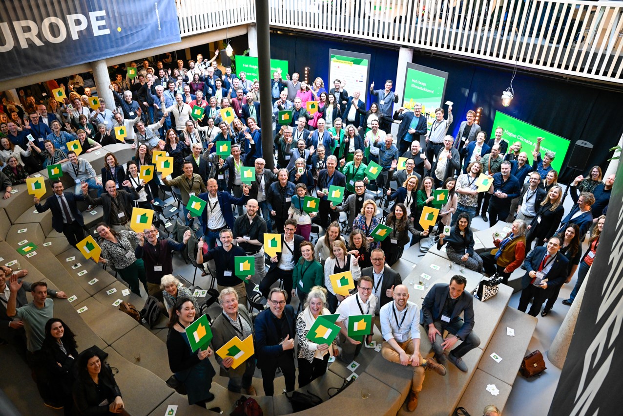 Een grote groep mensen houdt groene gele borden omhoog bij een evenement, met "EUROPE" op een banner.