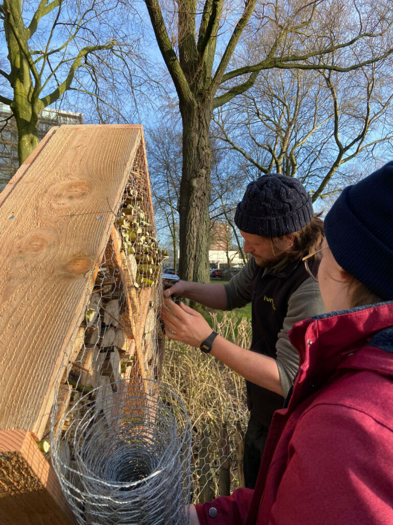 Een man bouwt een insectenhotel met gaas, buiten tussen bomen.