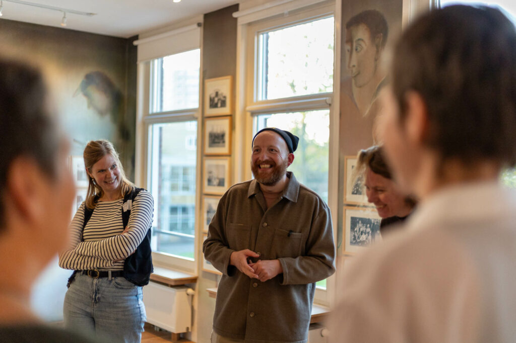 Groep mensen in een kunstgalerij, lachend en pratend bij ingelijste foto's aan de muur.