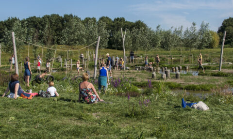 Mensen genieten van een zonnige dag in het park, spelend op een houten klimparcours met water.