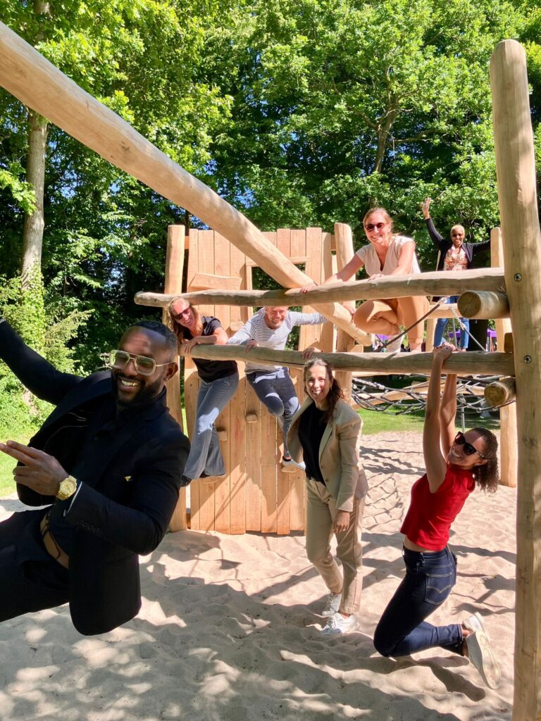 Groep volwassenen heeft plezier in een speeltuin met houten klimtoestel en zand.