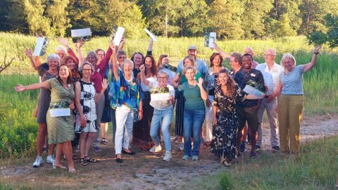 Groep mensen viert iets buiten met certificaten, in een groen natuurgebied.