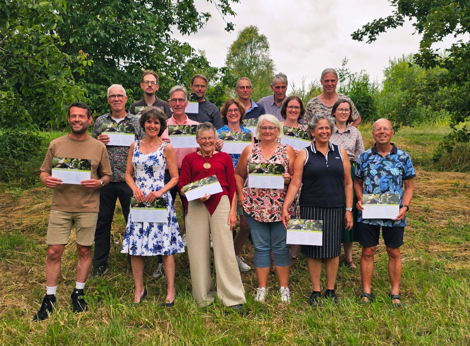 Groep mensen poseert buiten met certificaten, omringd door groen.