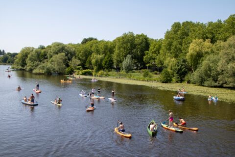 Mensen peddelen op SUP's en bootjes in een rivier, omgeven door groene bomen.