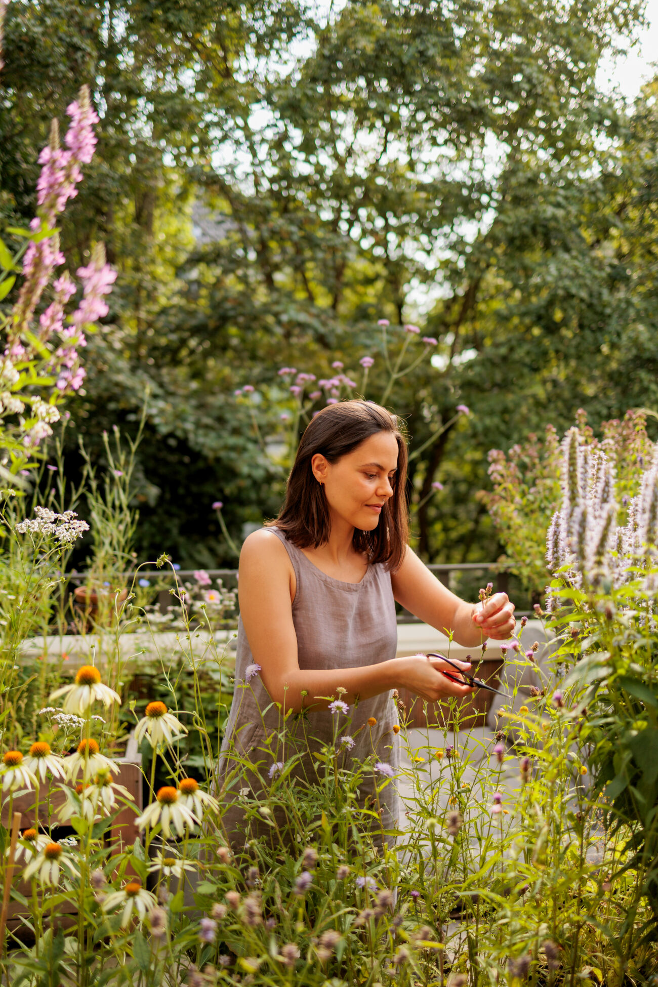 Vrouw verzorgt bloemen in een kleurrijke tuin, omringd door groen en bloeiende planten.
