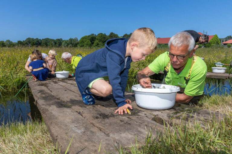 ivn vrijwilliger tijdens de slootjesdagen, kijkt in bak met jongen