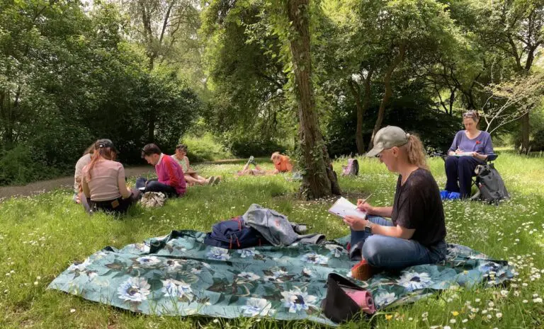 Mensen zitten op een kleed in een park, omgeven door bomen en gras, genietend van de natuur.