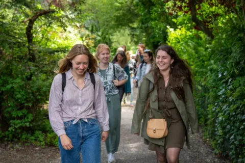 Groep lachende mensen loopt op een bosrijk pad met groene, dichtbegroeide omgeving.
