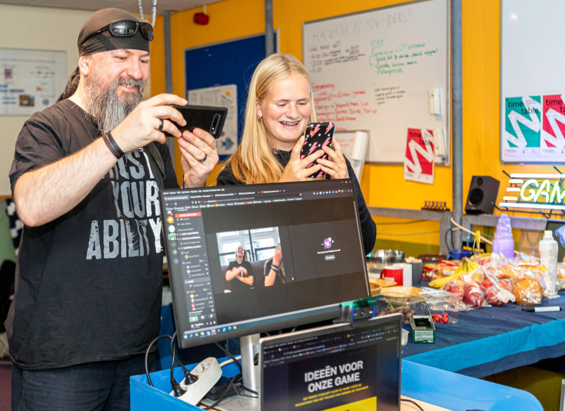 Twee mensen maken foto's in een kleurrijke ruimte met monitor en snacks op de achtergrond.