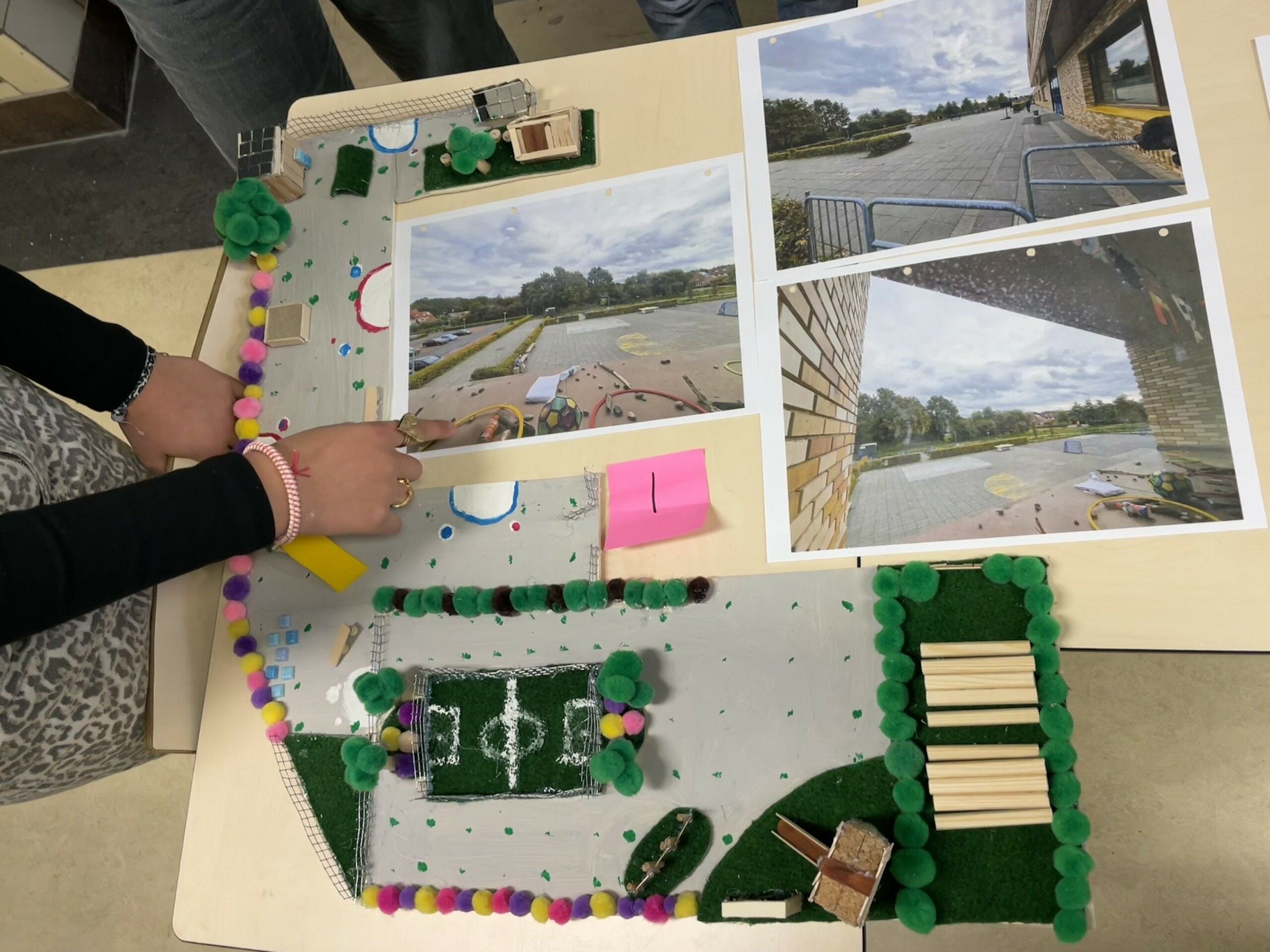 Maquette en foto's van een pleinontwerp, met een hand die naar details wijst.