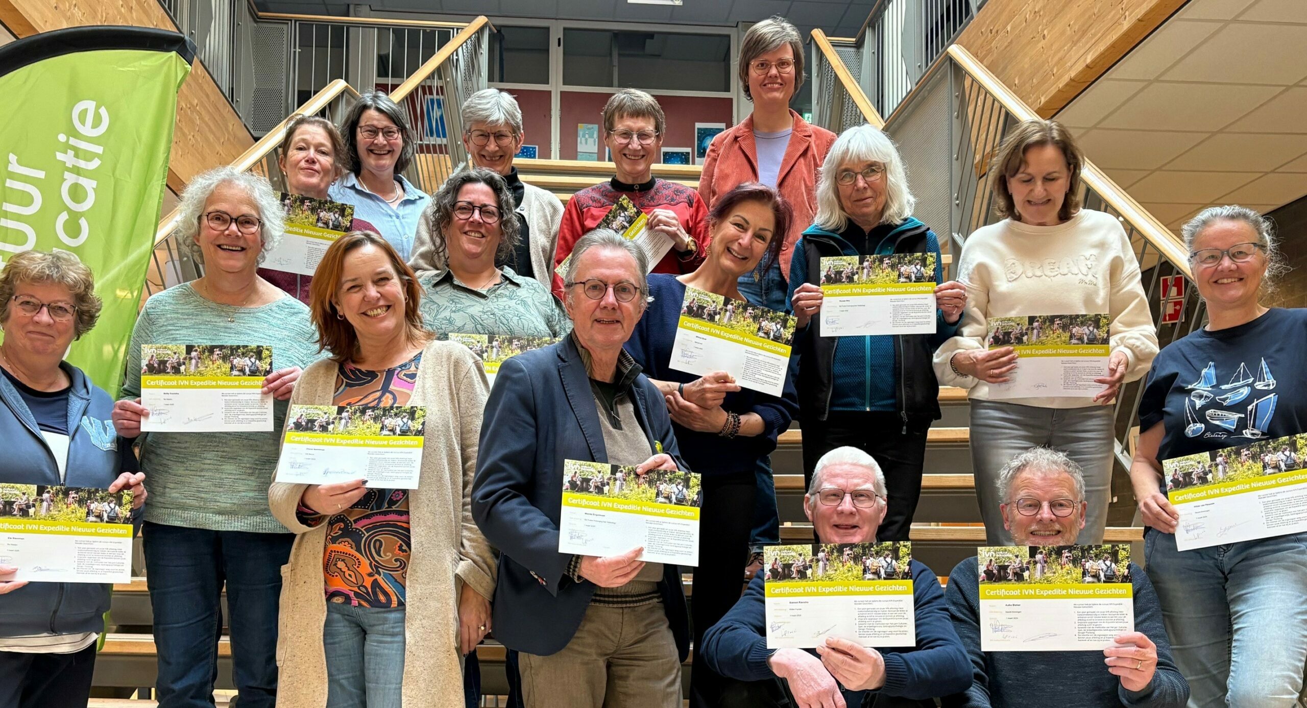 Groep mensen op een trap houdt certificaten vast voor IVN Expeditie Nieuwe Gezichten, met een groene vlag links.