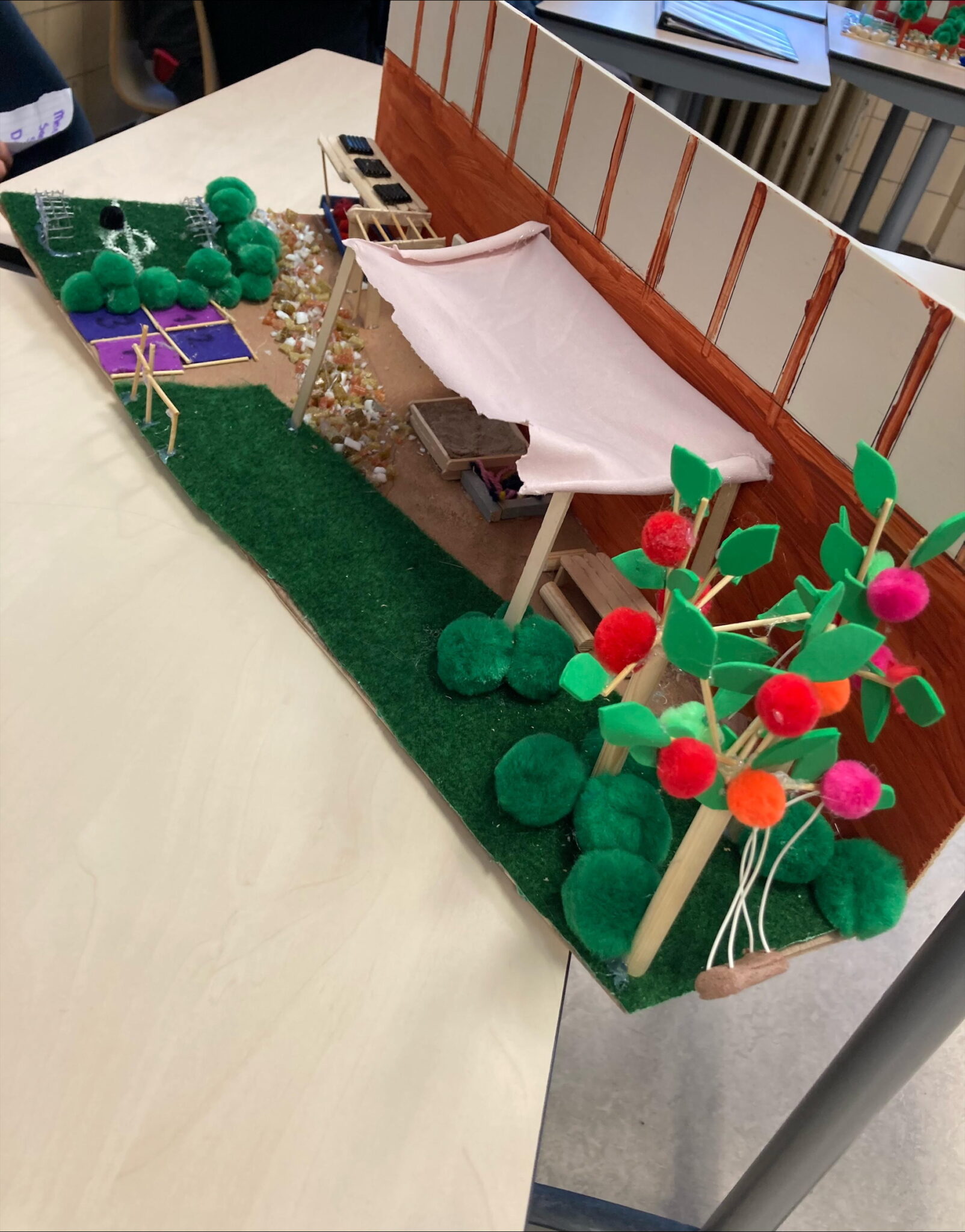 Miniatuurtuin met schuur, paden van grind, bomen met pompons en een groen grasveld.