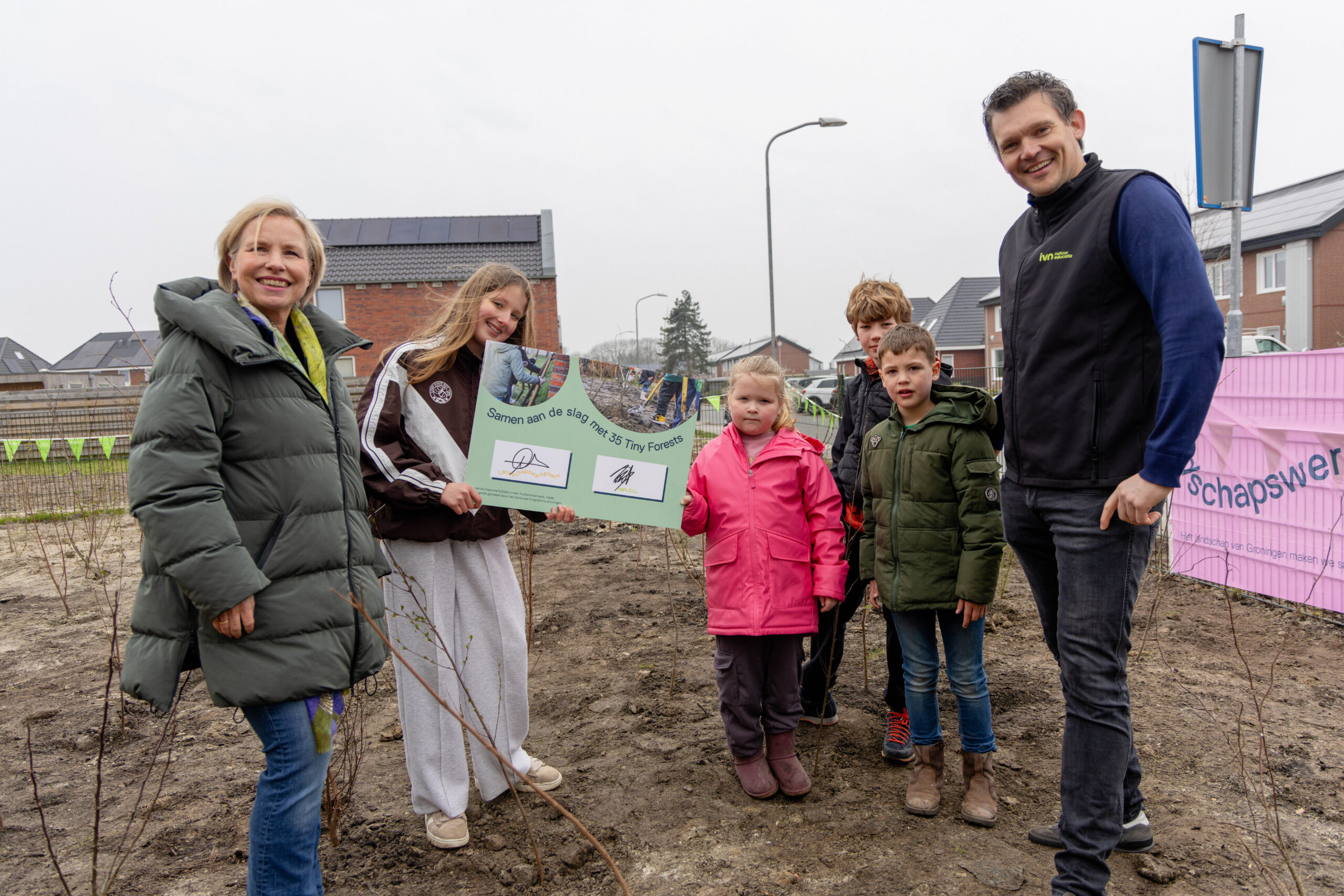 Een groep mensen plant bomen met een bord "Samen aan de slag met 35 Tiny Forests".