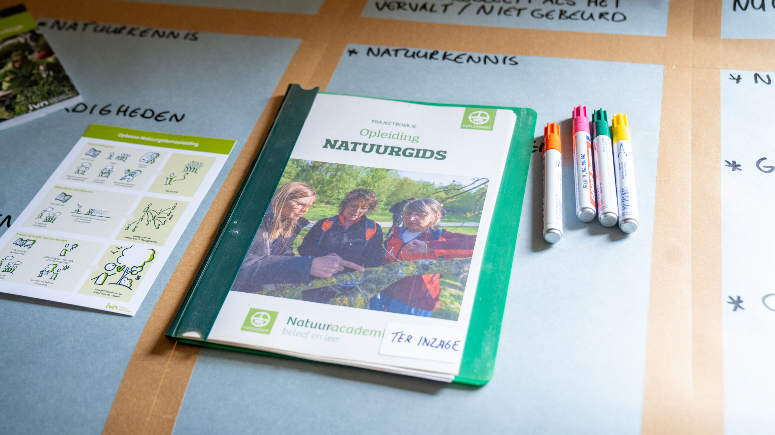 Handleiding voor natuurgidsopleiding en pennen op een tafel met notities.