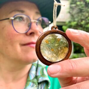 Persoon houdt een handgemaakte ronde hanger voor groene achtergrond vast.