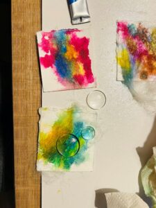 Kleurrijke aquareltests op keukenpapier, met een verf tube en glazen cirkels erop geplaatst.