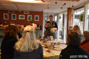 Persoon demonstreert kunsttechniek aan groep in een knutselruimte met kunstwerken aan de muur.