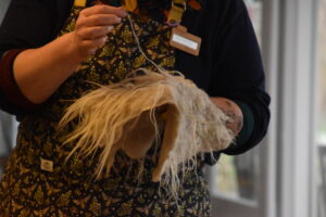 Persoon houdt een vilten object vast, gekleed in een patroon schort met bladmotief.