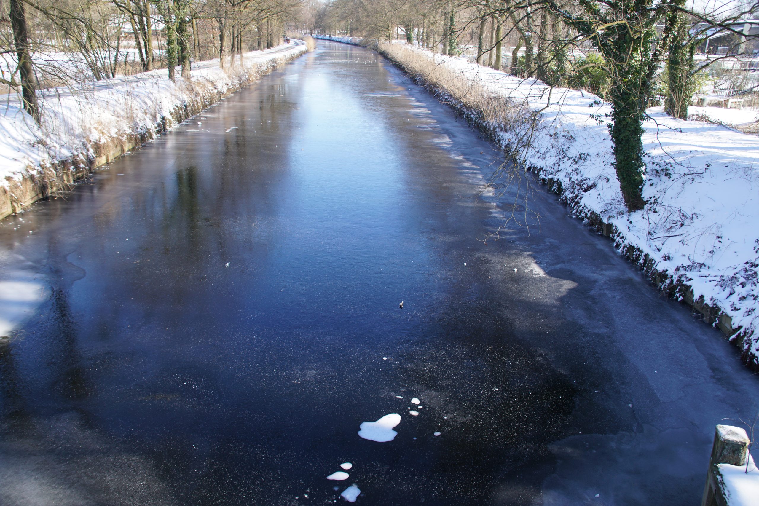 Bevroren kanaal met sneeuwbedekte oevers en bomen in een winterlandschap.
