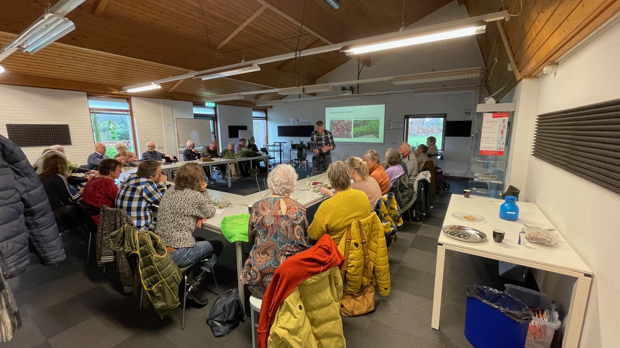 Groepsbijeenkomst in een vergaderruimte, presentatie over tuinieren voor een zittend publiek.