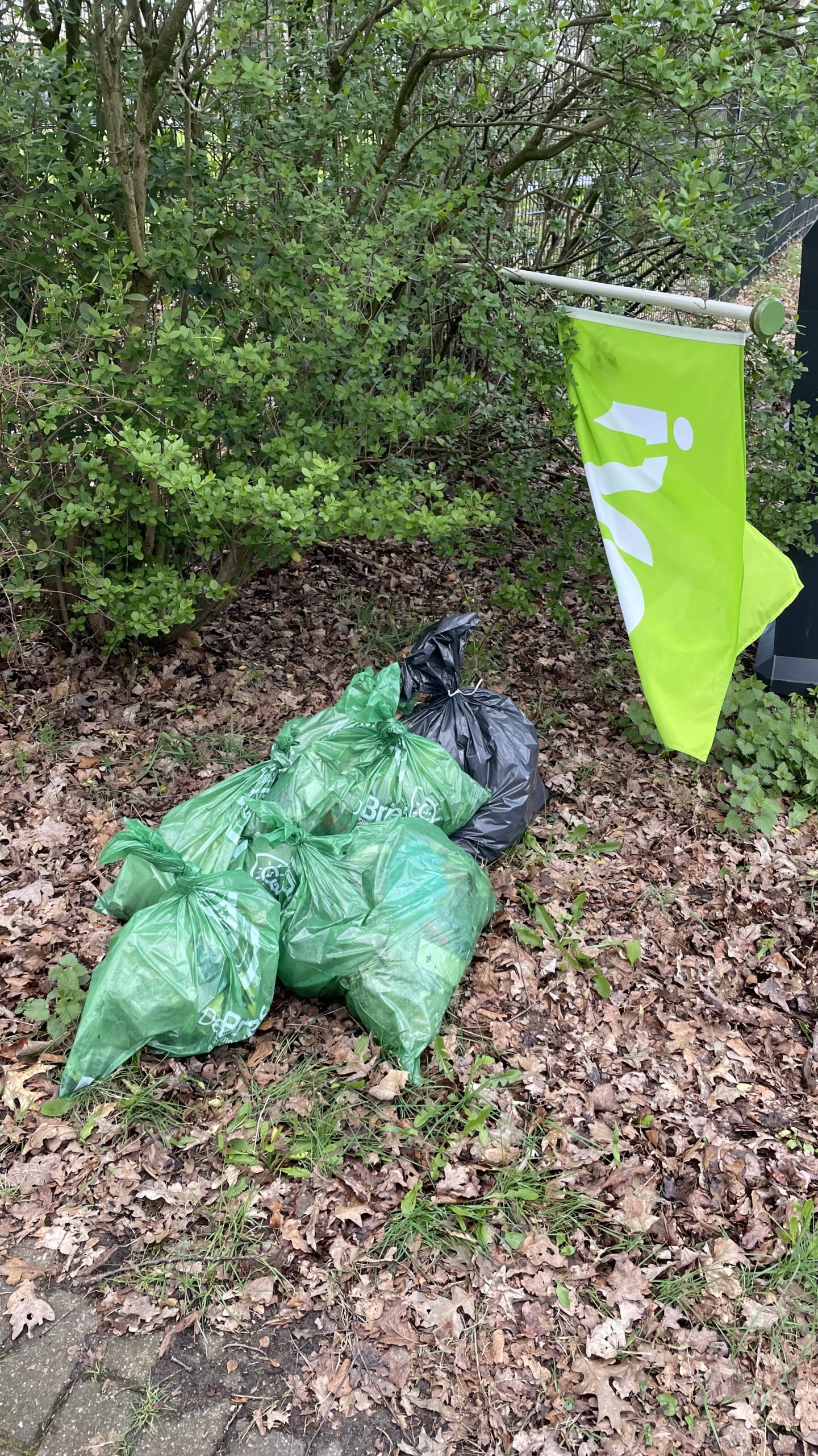 Groene en zwarte vuilniszakken naast een groene vlag in een bosrijke omgeving.