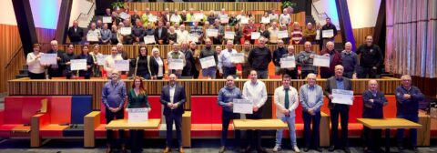 Een grote groep mensen houdt certificaten vast in een auditorium.