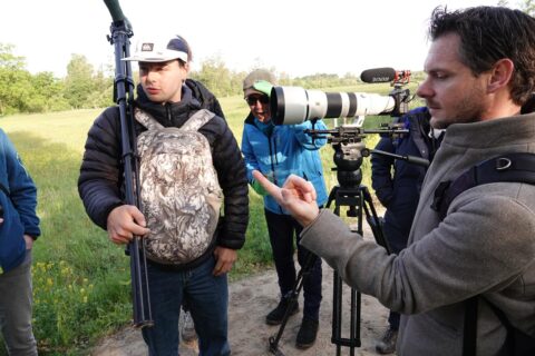 Groep mannen met camera-apparatuur buiten in een veld, gefocust op natuurfotografie.