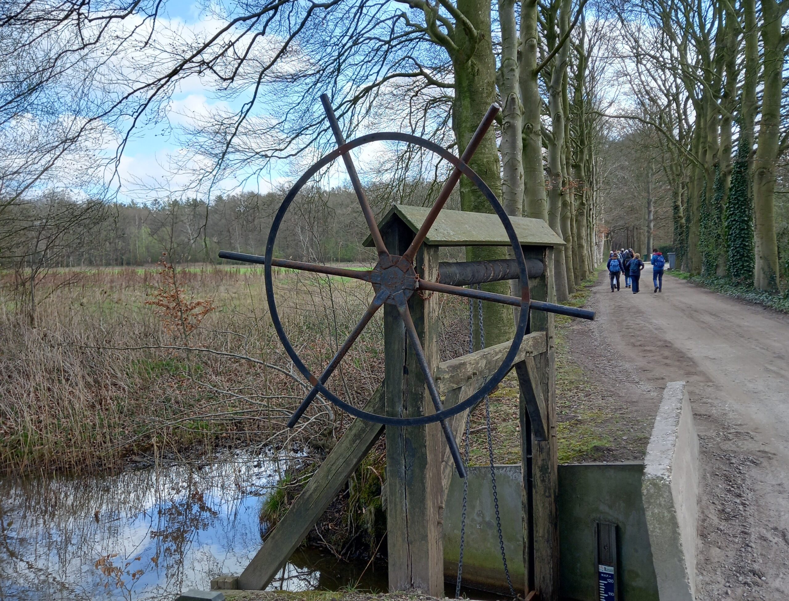 Oude watermolen in bosrijke omgeving, met wandelaars op het pad naast de molen.