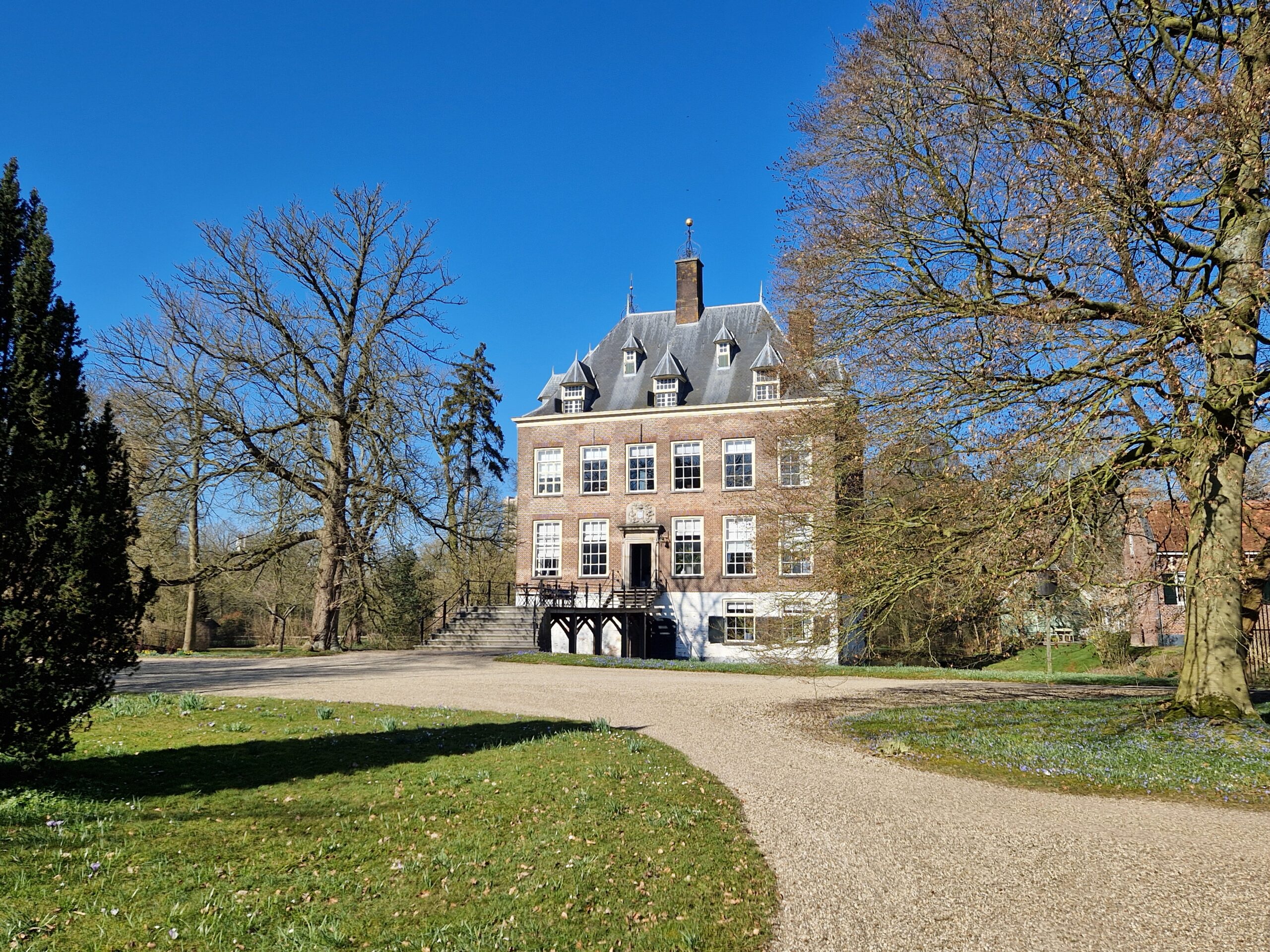 Historisch gebouw met trapgevels, omringd door kale bomen, onder een heldere blauwe hemel.