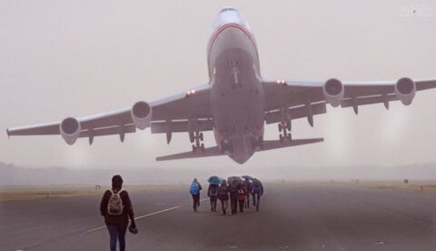 Een groot vliegtuig stijgt op, terwijl mensen over de landingsbaan lopen.