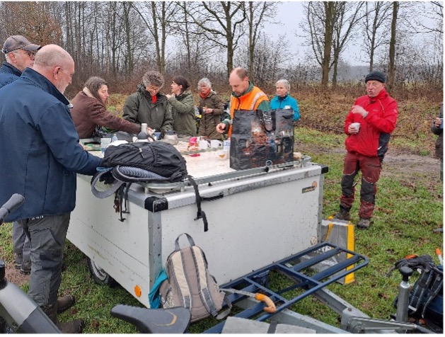 Een groep mensen drinkt koffie rond een mobiele kar in een winters bos.