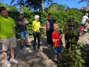 Groep mensen kijkt naar planten op een zonnige dag in een parkachtige omgeving.