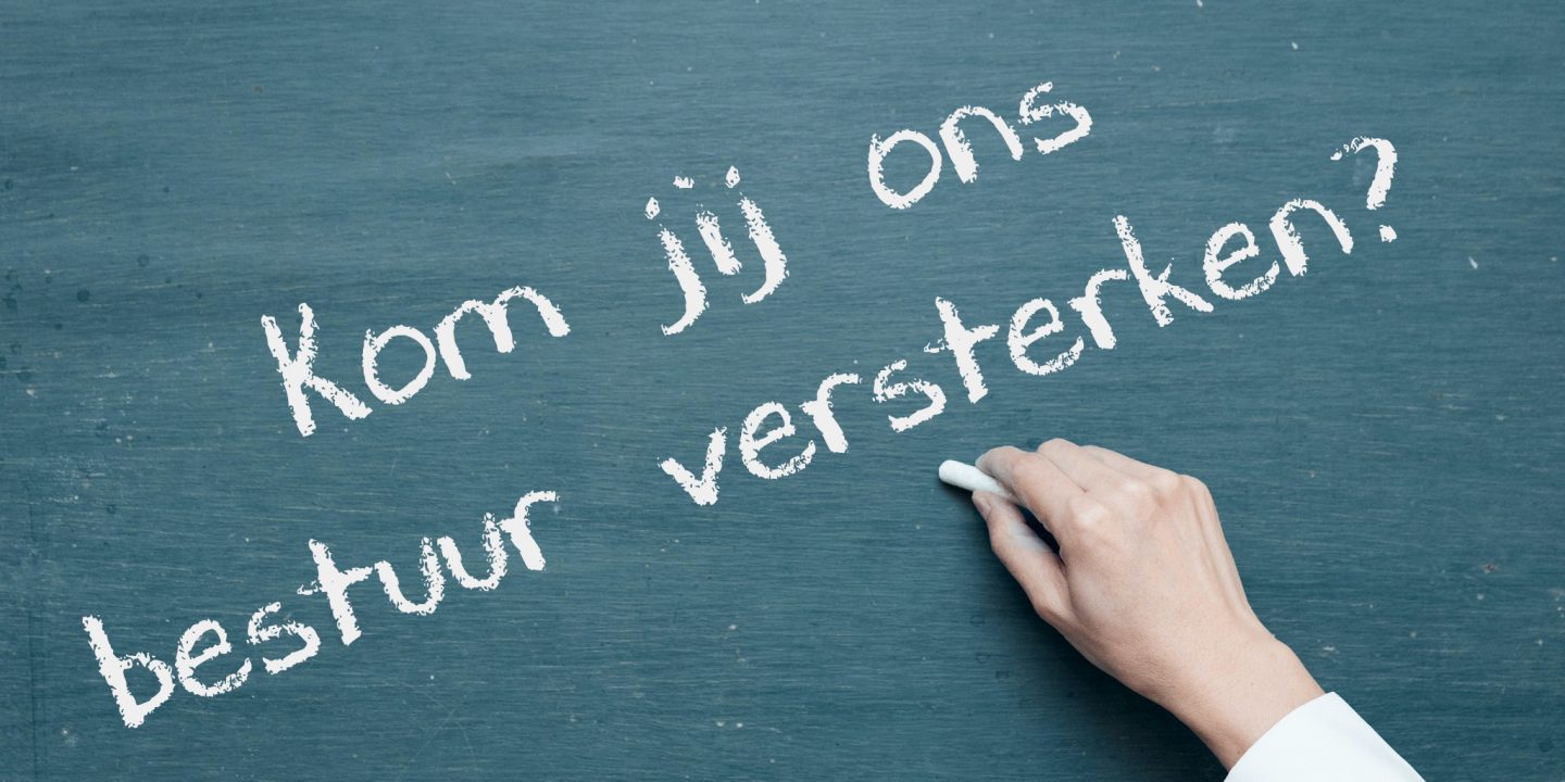 Hand schrijft op groen schoolbord: "Kom jij ons bestuur versterken?"