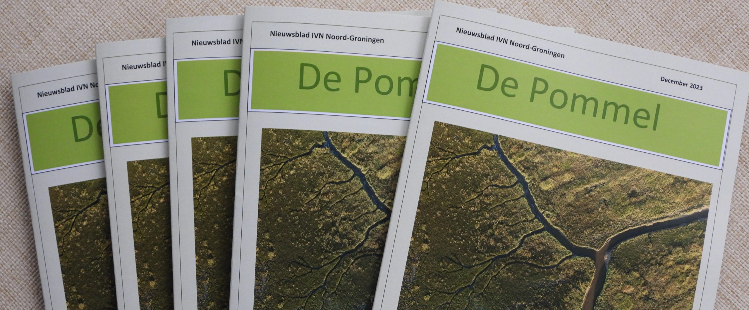 Vijf exemplaren van "De Pommel" nieuwsblad, december 2023, met luchtfoto op de omslag.