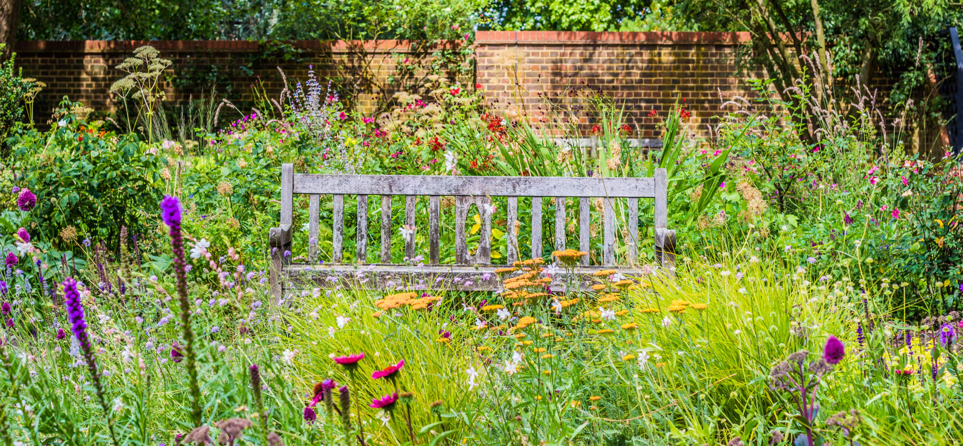 Houten bank in kleurrijke bloementuin met bakstenen muur op achtergrond.