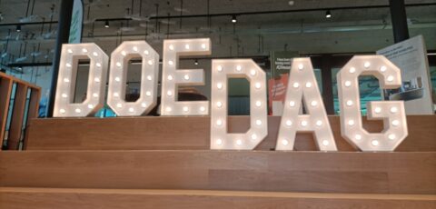 Verlichte letters op een trap vormen het woord "DOEDAG" in een binnenruimte.