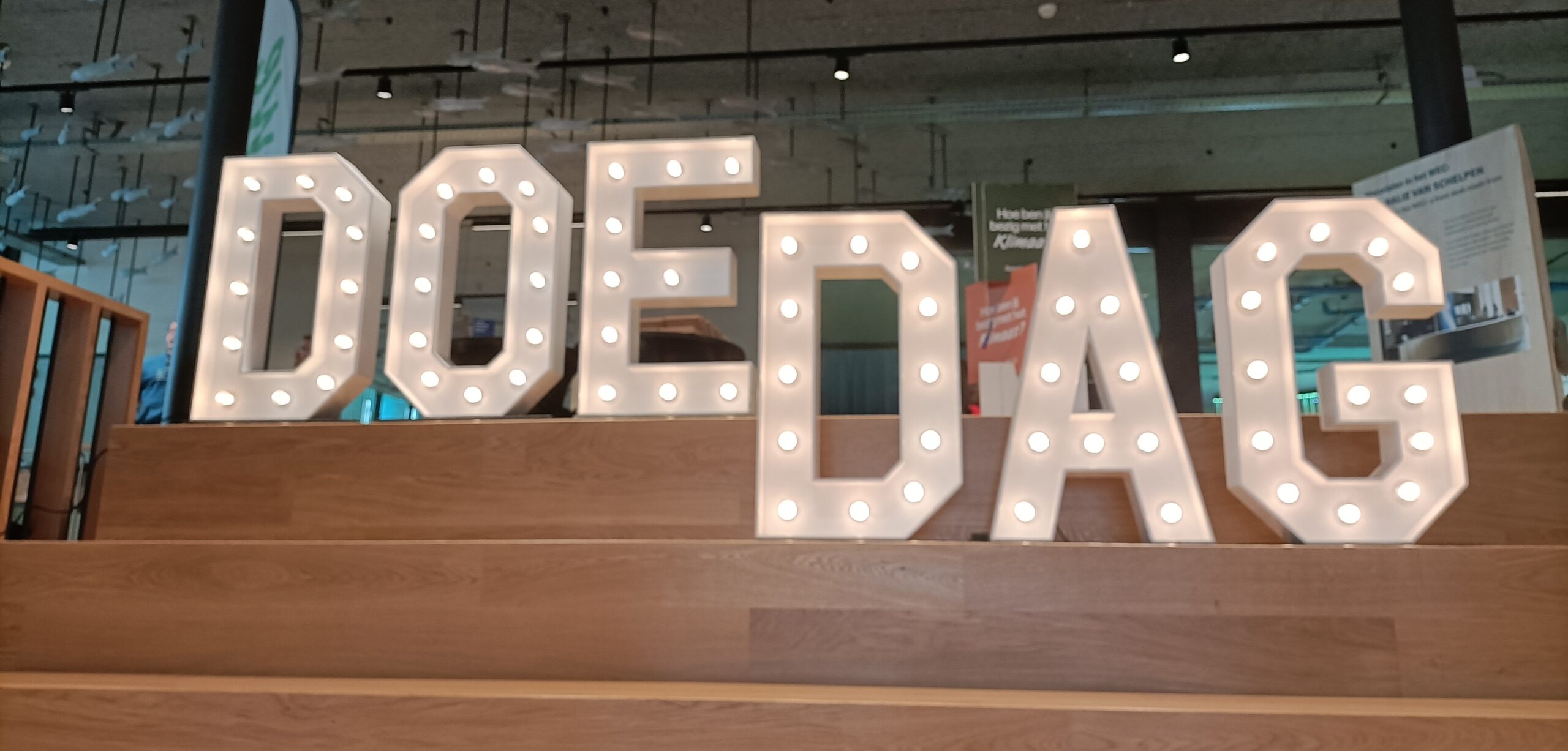 Verlichte letters op een trap vormen het woord "DOEDAG" in een binnenruimte.