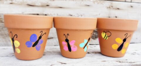 Drie terracotta bloempotten met kleurrijke vlinder- en bijenmotieven geschilderd erop.