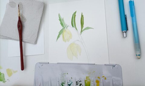 Papier met een halfafgemaakte aquarel van bloemen, penseel en pennen ernaast.