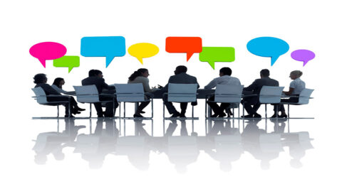 Vergaderende mensen aan tafel met gekleurde tekstballonnen boven hoofden, witte achtergrond.