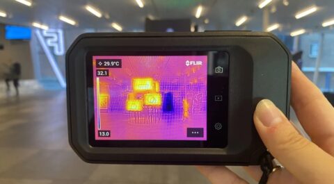 Thermische camera toont warme objecten in een moderne ruimte. Scherm leest 29.9°C.