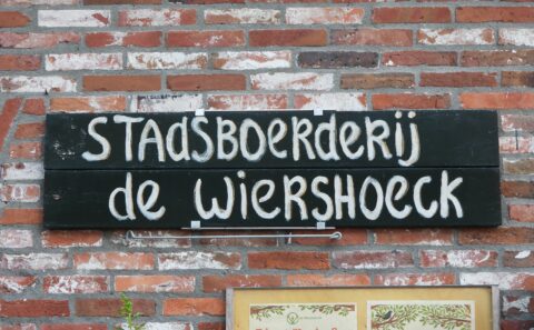 Bord op bakstenen muur met tekst: "Stadsboerderij de Wiershoeck".