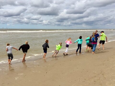 Kinderen spelen hand in hand op een winderig strand onder een bewolkte hemel.