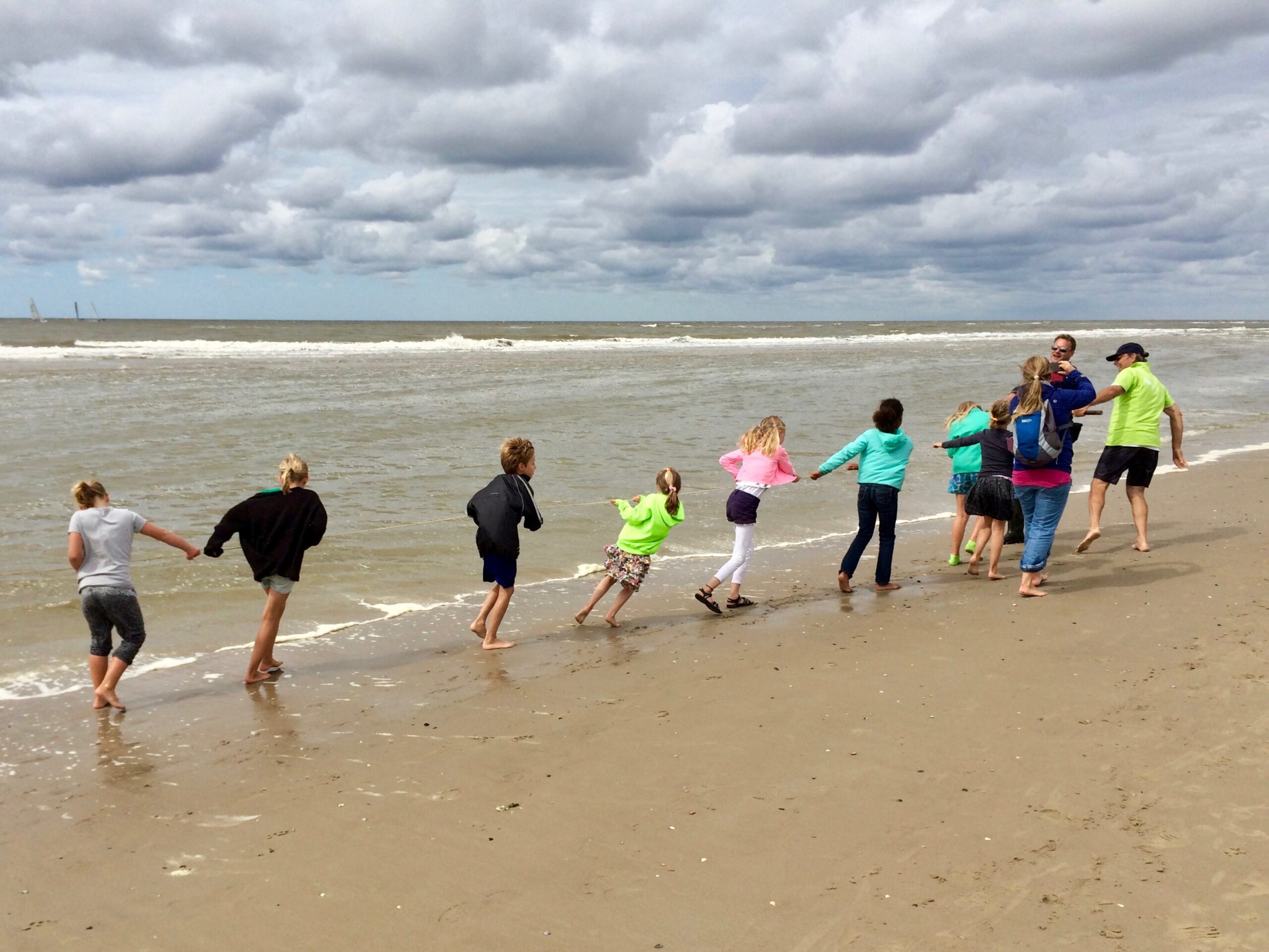 Kinderen spelen hand in hand op een winderig strand onder een bewolkte hemel.